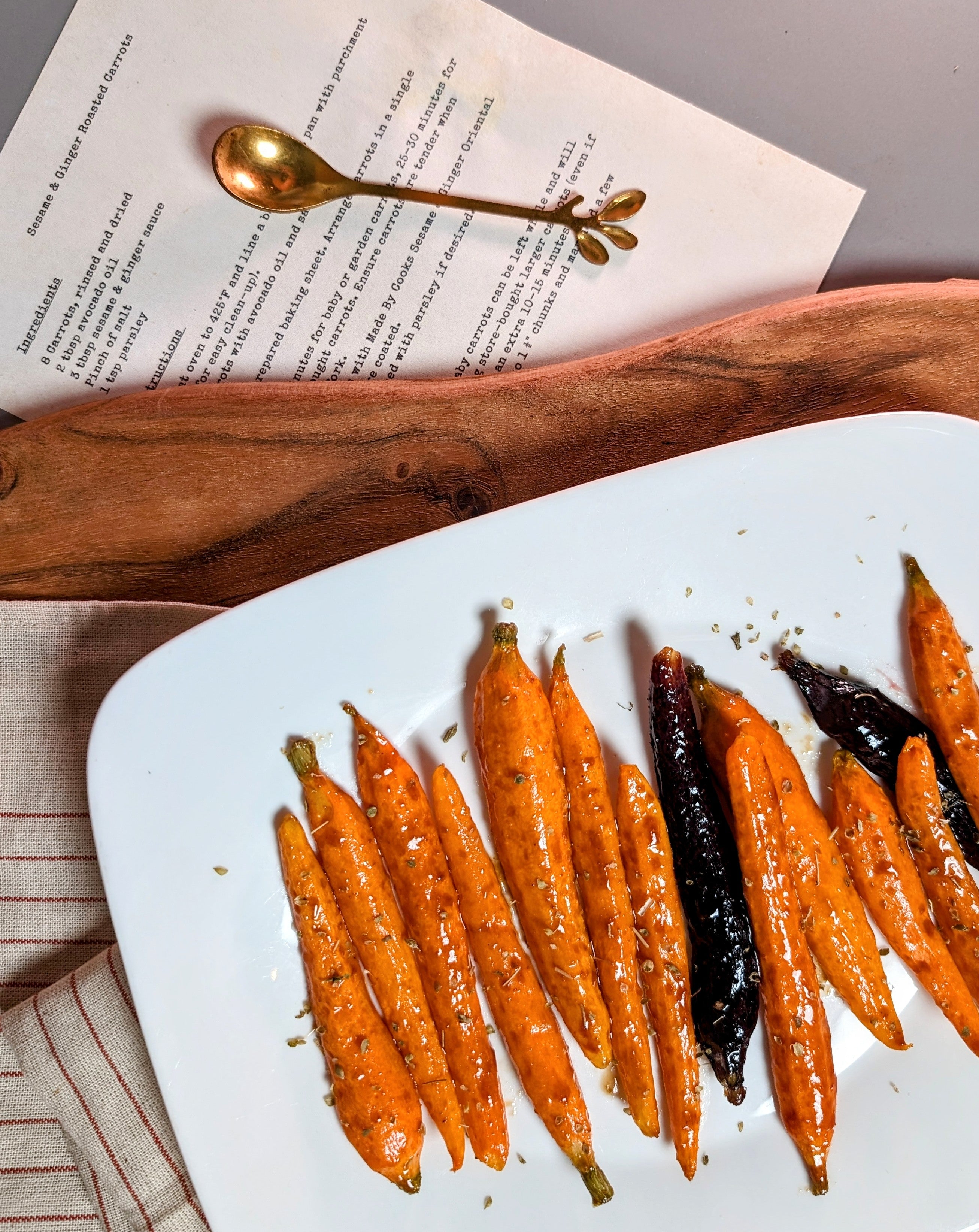 Sesame & Ginger Sauce coated roasted carrots with recipe page and wooden cutting board.